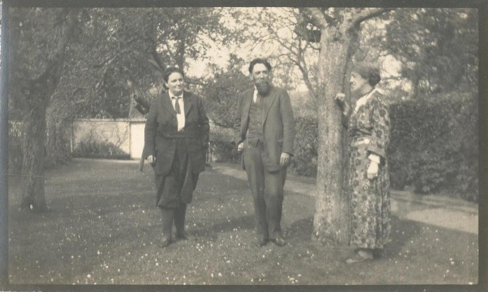 Photo en noir et blanc de deux femmes debout de chaque côté d'un homme barbu.  May est à droite dans une robe à fleurs tandis que Mary est à gauche vêtue d'un tailleur-pantalon foncé.
